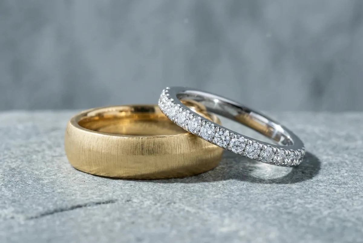 A pair of wedding bands, a brushed yellow gold men's band and a diamond-set white gold women's band, resting together