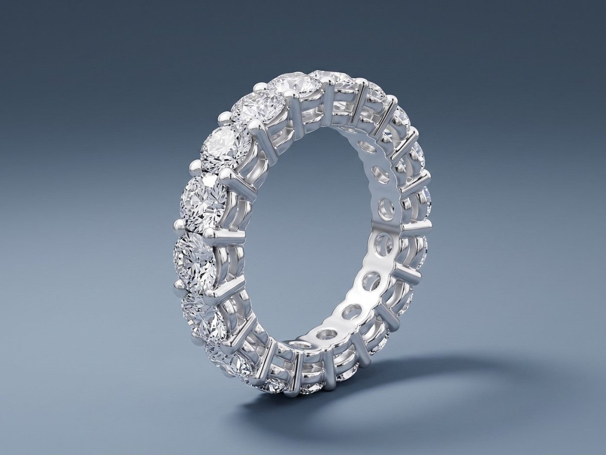 A round diamond eternity band in white gold standing on a slate blue studio ground