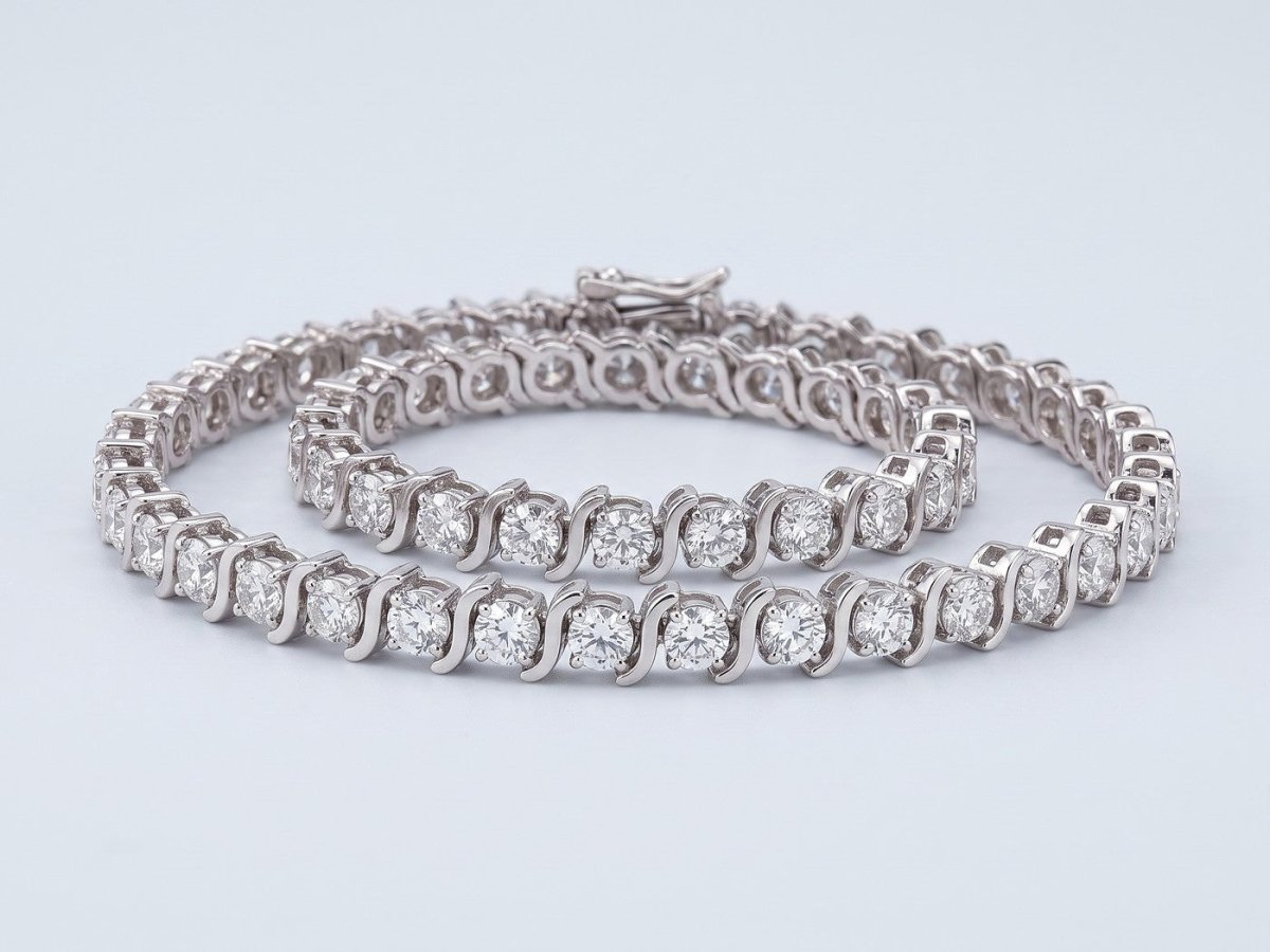 A round diamond tennis bracelet in white gold, coiled on a pale grey studio ground
