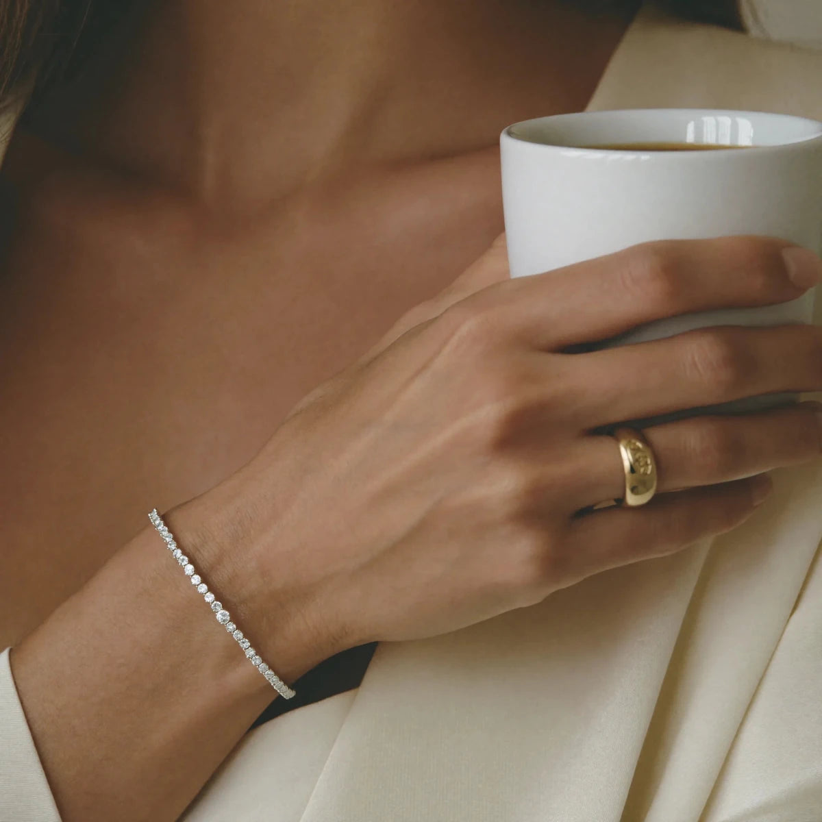 A wrist wearing a delicate diamond bracelet while holding a coffee cup