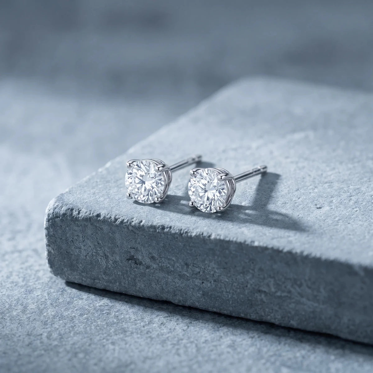 A pair of diamond solitaire studs on a stone plinth
