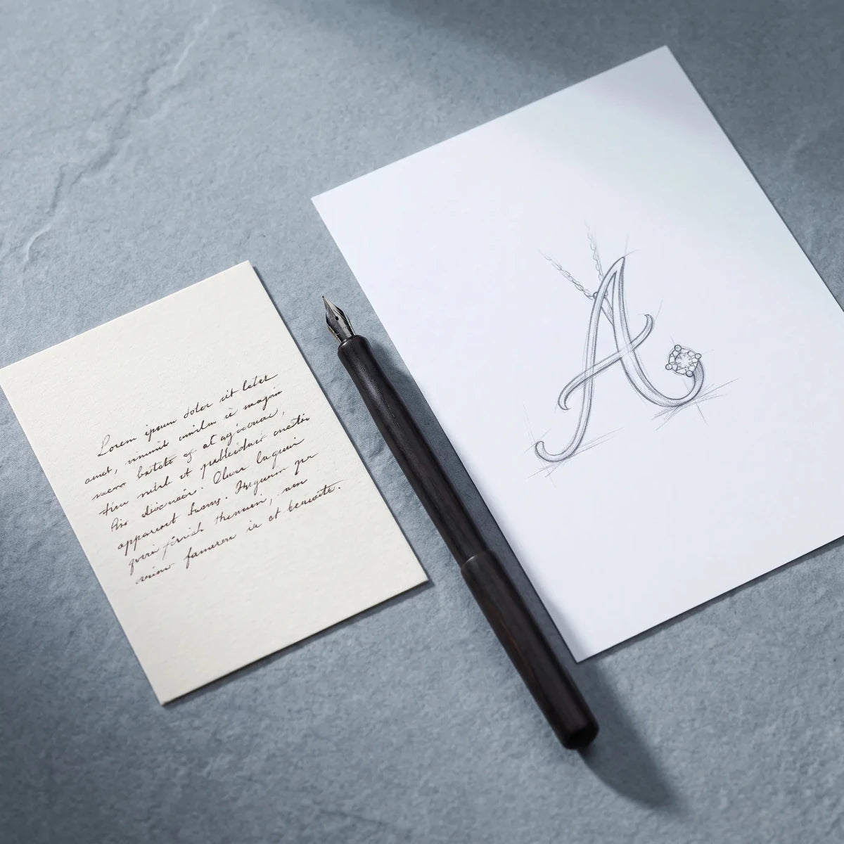 A handwritten note beside a pencil sketch of an initial pendant