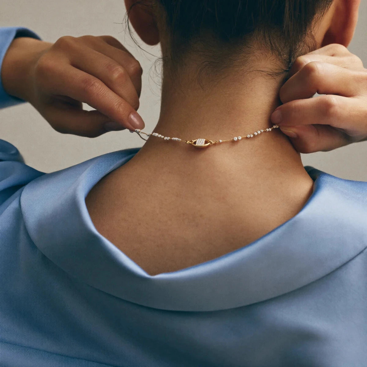 Hands fastening a delicate necklace at the back of the neck