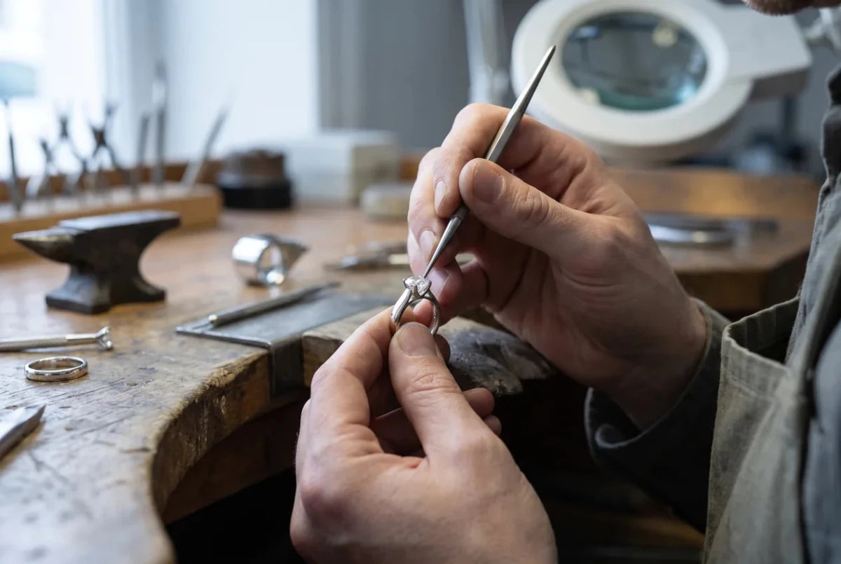 A jeweler's hands setting a round diamond into a white gold ring head at the bench