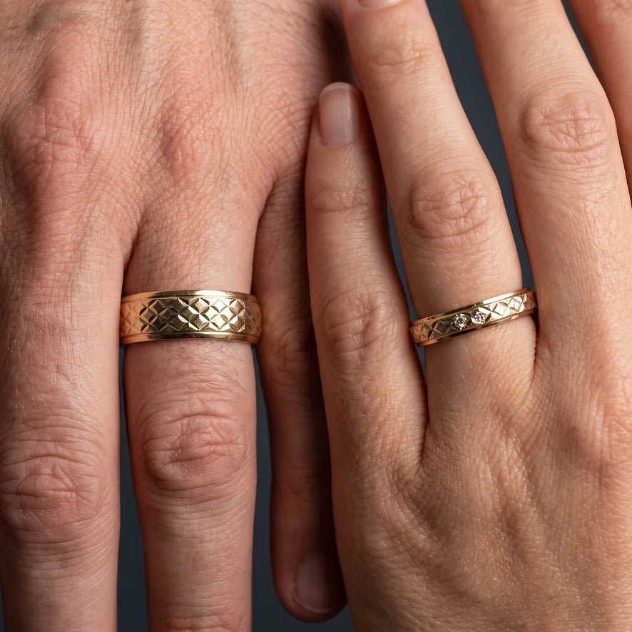 Two hands side by side wearing matching gold rings of different widths, same pattern