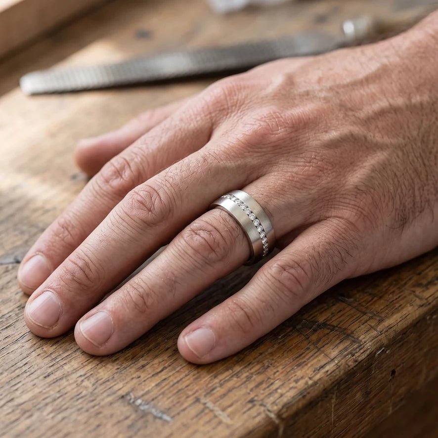 A man's hand wearing a wide low-profile diamond band, resting on a workbench