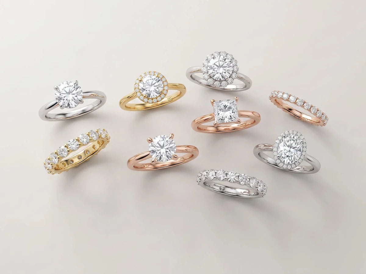 Diamond engagement rings and wedding bands arranged on a neutral surface, photographed from above the bench behind her