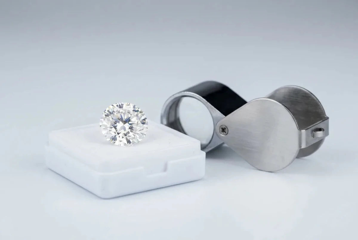 A round diamond on a grading tray beside a jeweler's loupe