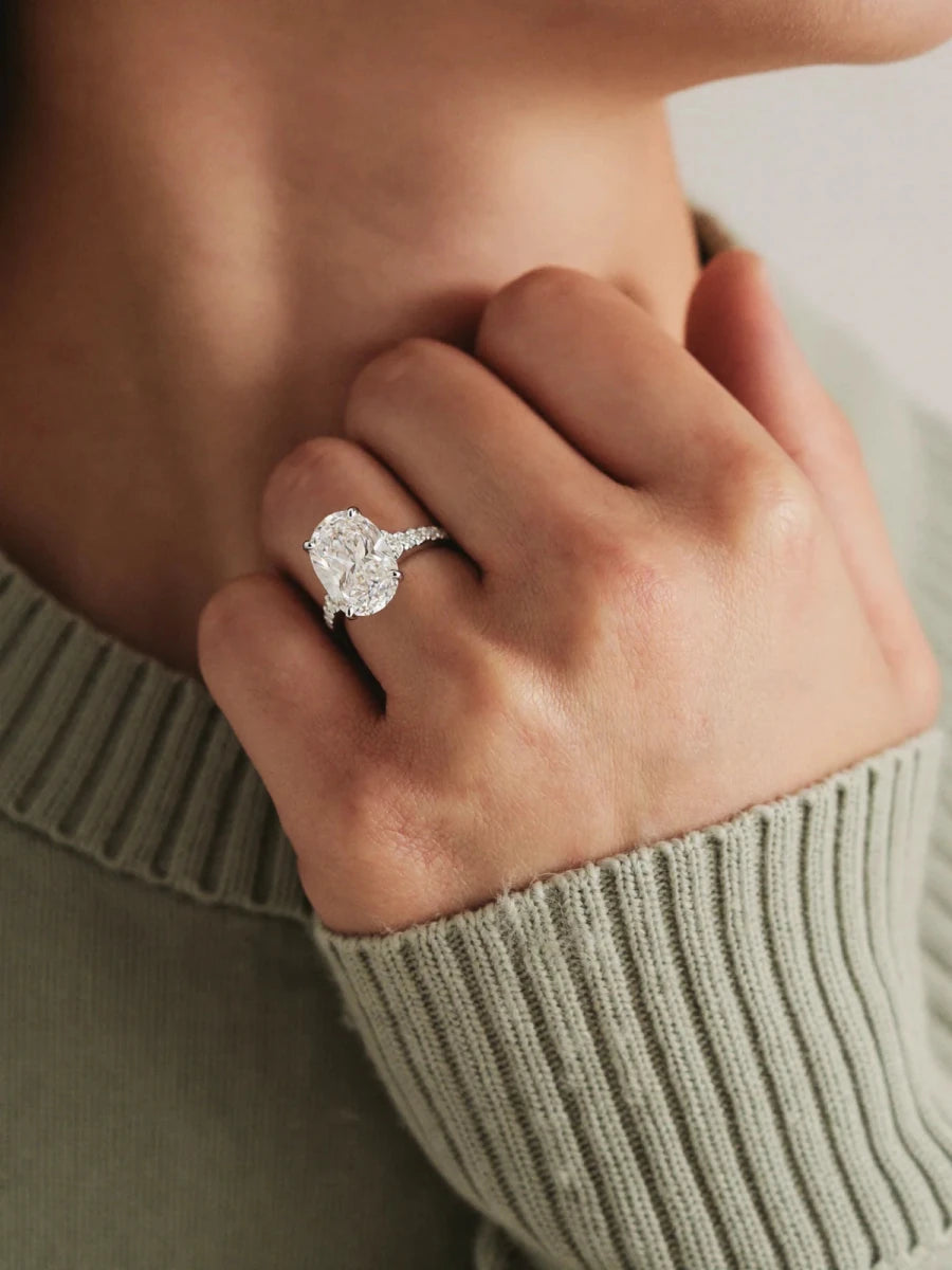An oval diamond ring in white gold worn on her hand, resting against a sage green knit sweater