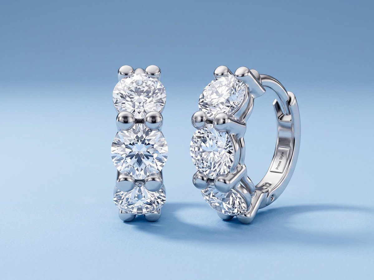 A pair of white gold huggie hoop earrings set with three round diamonds each, on powder blue