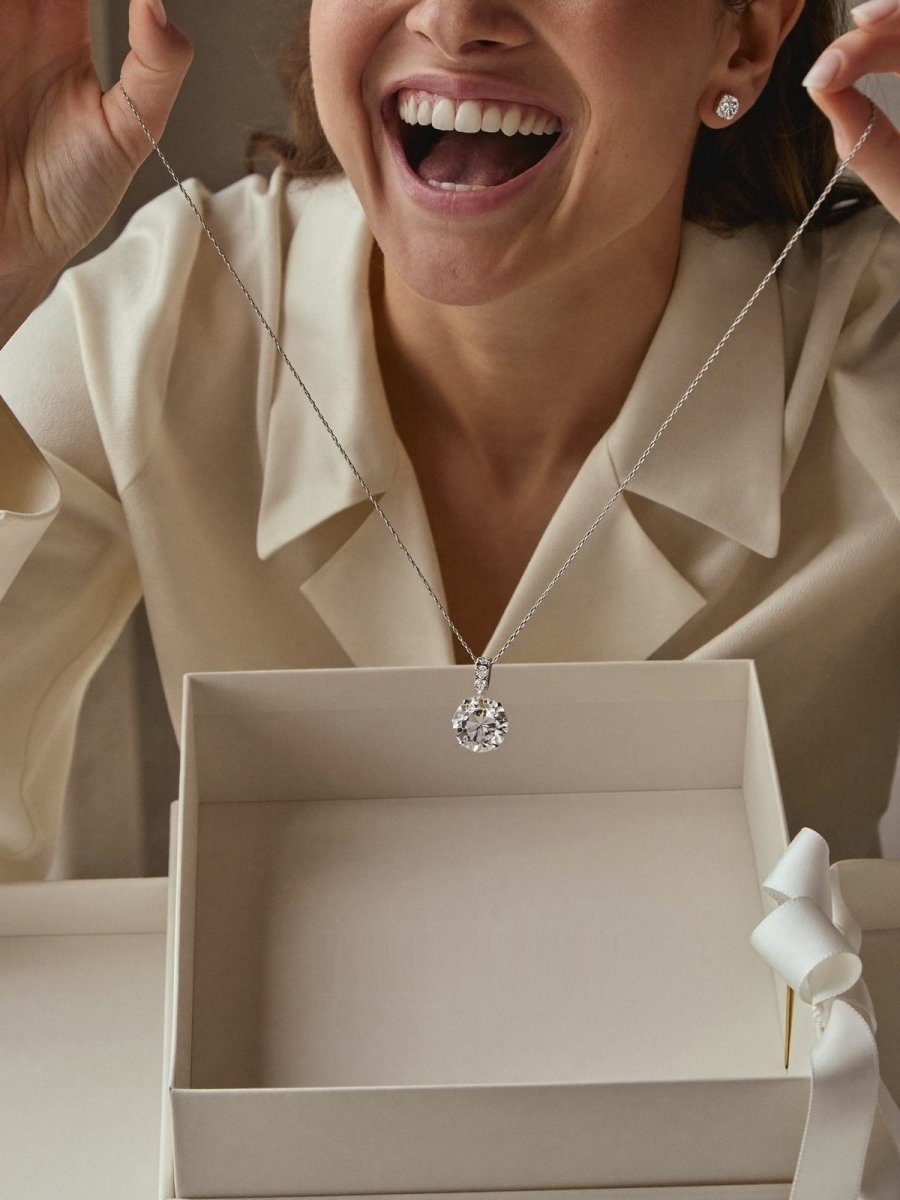 A delighted woman lifting a diamond pendant necklace out of an elegant gift box