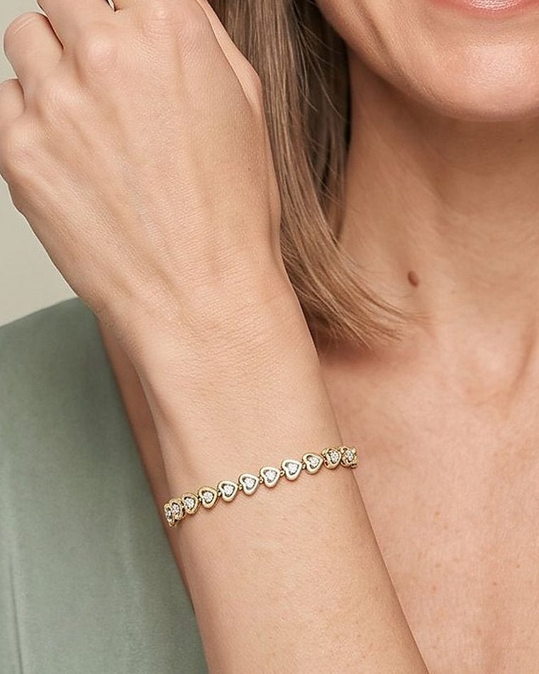 A woman in sage green raising her wrist, wearing a yellow gold diamond bracelet