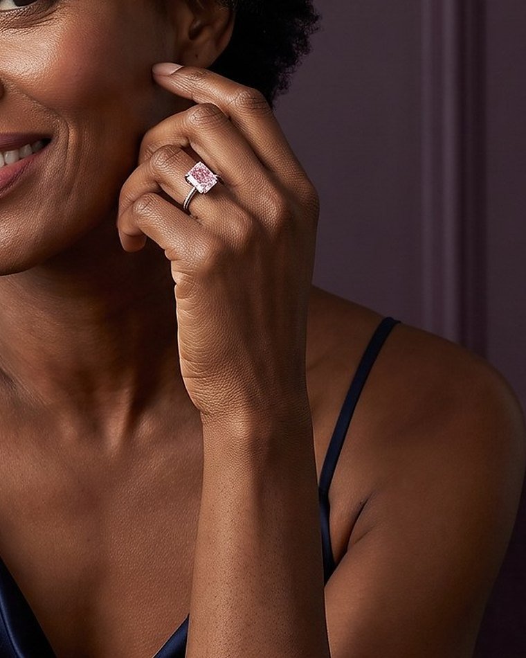 A woman in a navy dress touching her ear, wearing a fancy pink diamond ring
