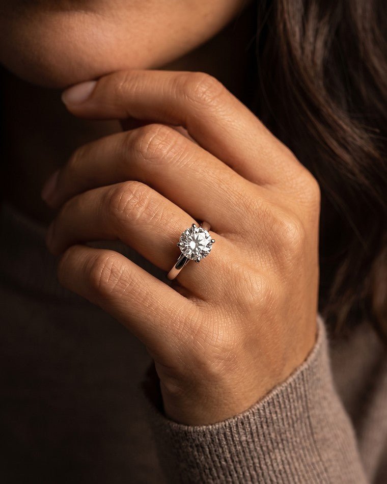 A white gold round diamond solitaire engagement ring worn on a woman's hand