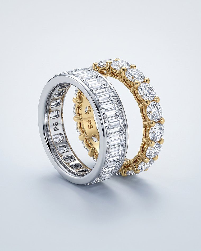 An emerald cut white gold eternity band beside a round yellow gold eternity band
