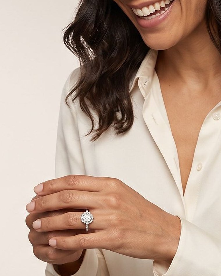A woman in a cream silk blouse resting her hand on her sleeve, wearing a halo diamond engagement ring