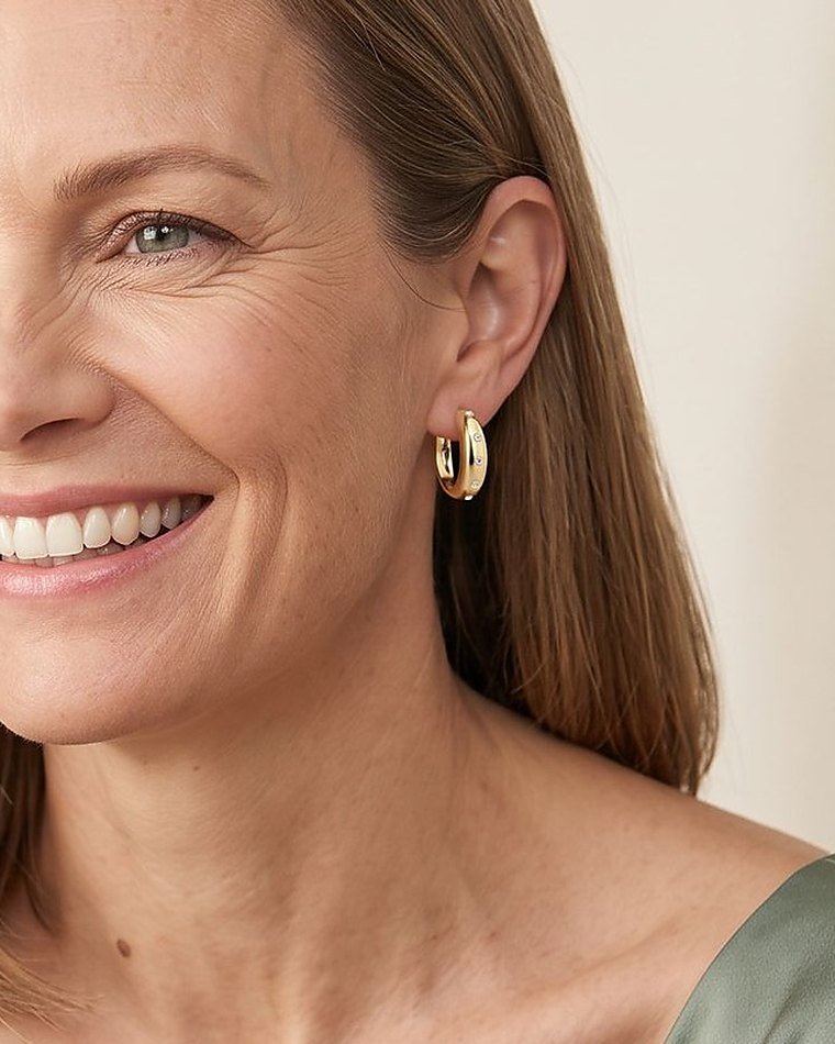 A smiling woman in sage green, wearing gold diamond hoop earrings