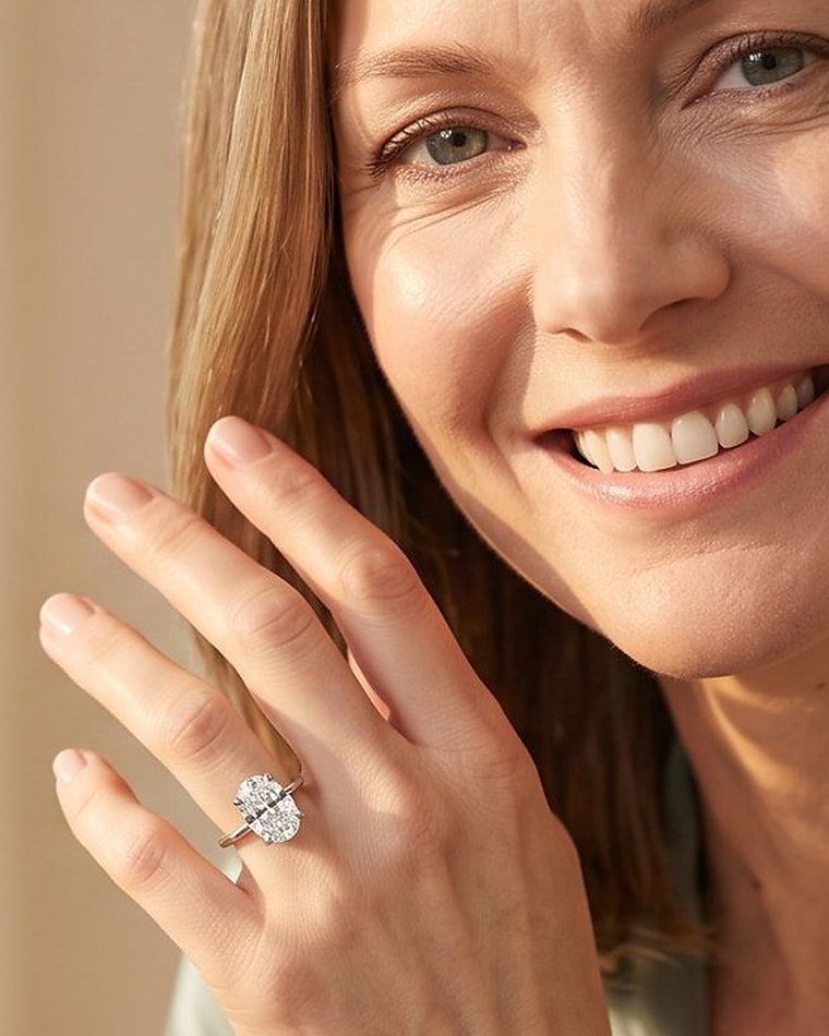 A smiling woman with her hand at her cheek, wearing an oval lab grown diamond engagement ring