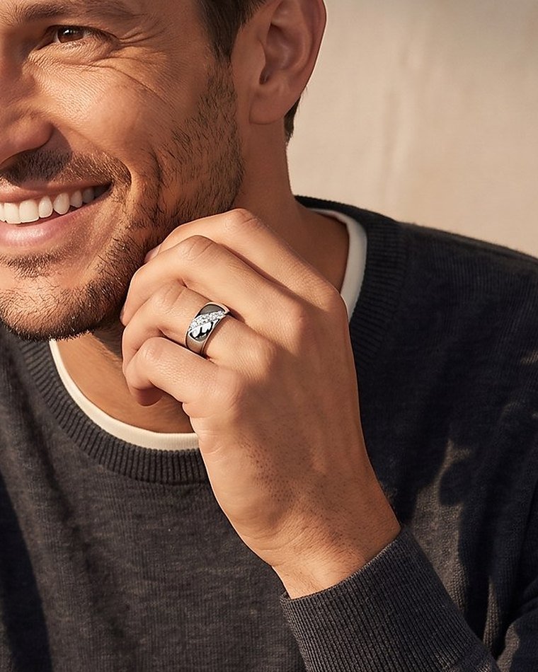 A smiling man in a navy sweater with his hand at his jaw, wearing a diamond wedding band