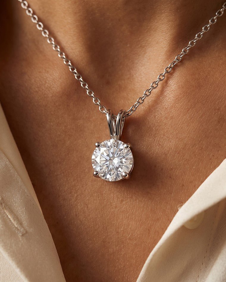 A white gold round diamond solitaire pendant worn at a woman's throat