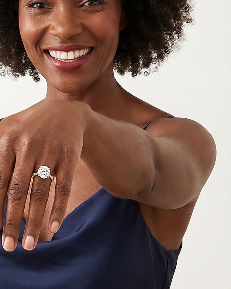 A laughing woman in a navy dress showing a diamond engagement ring on her hand