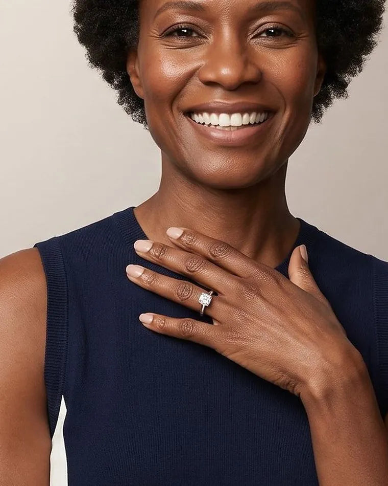 A laughing woman in a navy dress with her hand on her chest, wearing a solitaire diamond engagement ring
