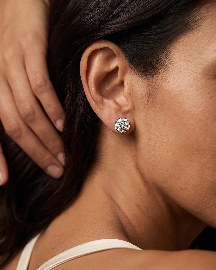A white gold round diamond stud earring worn on a woman's ear
