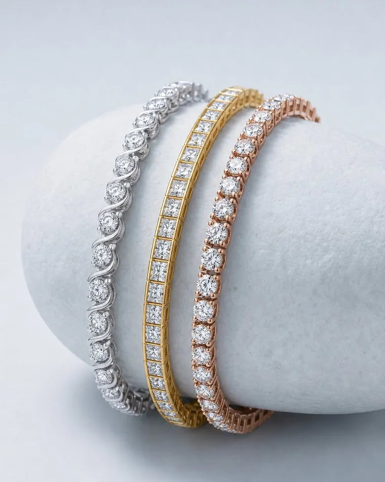 Three best-selling diamond tennis bracelets, an S-link in white gold, a princess-cut channel set in yellow gold and a four-prong round in rose gold, over a pale stone