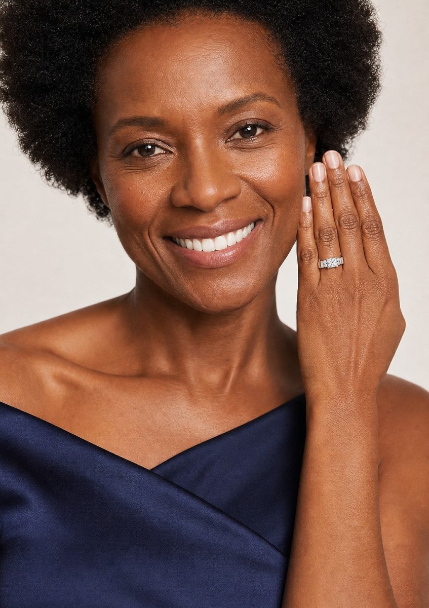A smiling woman in a navy and ivory off the shoulder dress with her hand at her collarbone, wearing a yellow gold diamond bridal set