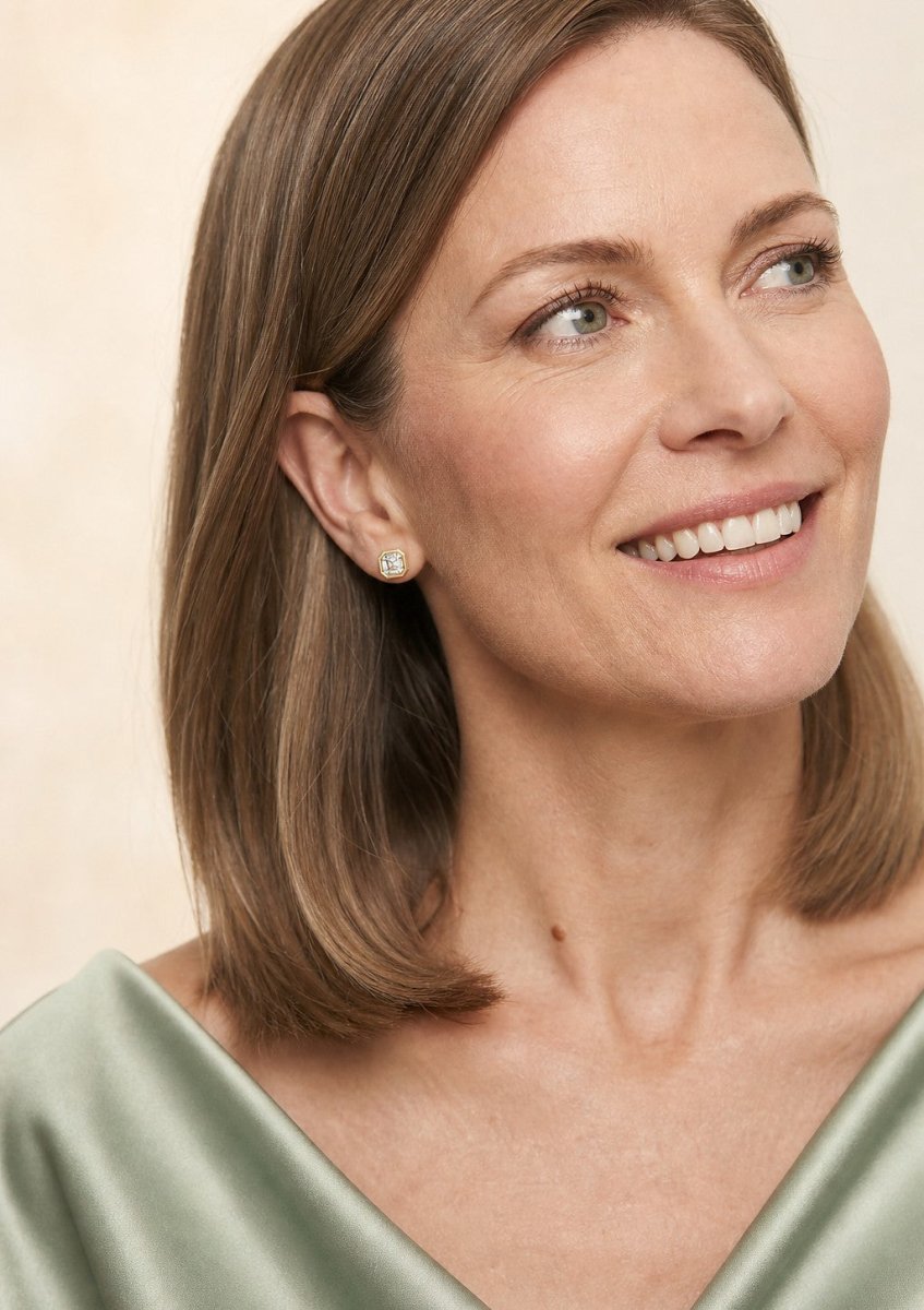 A smiling woman wearing a yellow gold earrings set with square asscher cut, with cut corners and concentric step facets diamonds