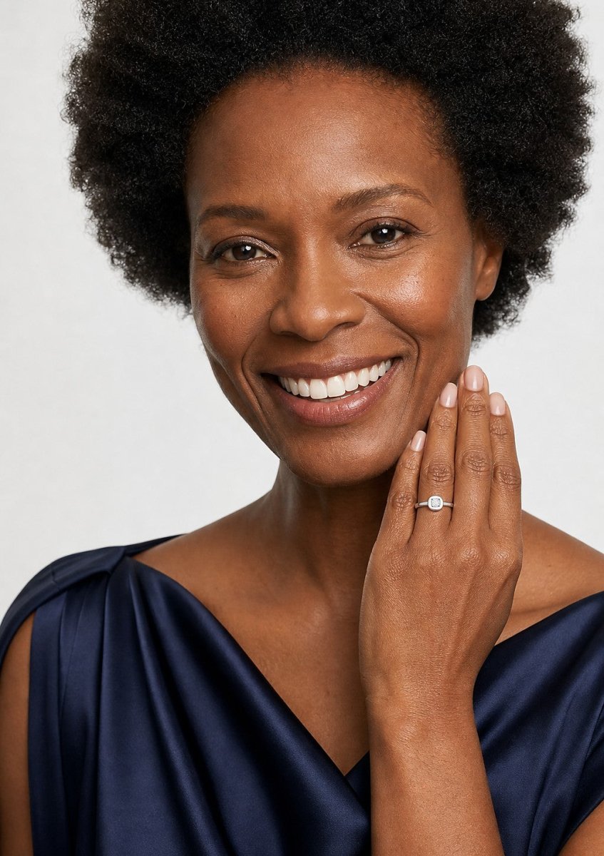 A smiling woman wearing a white gold ring set with softly rounded square cushion cut diamonds