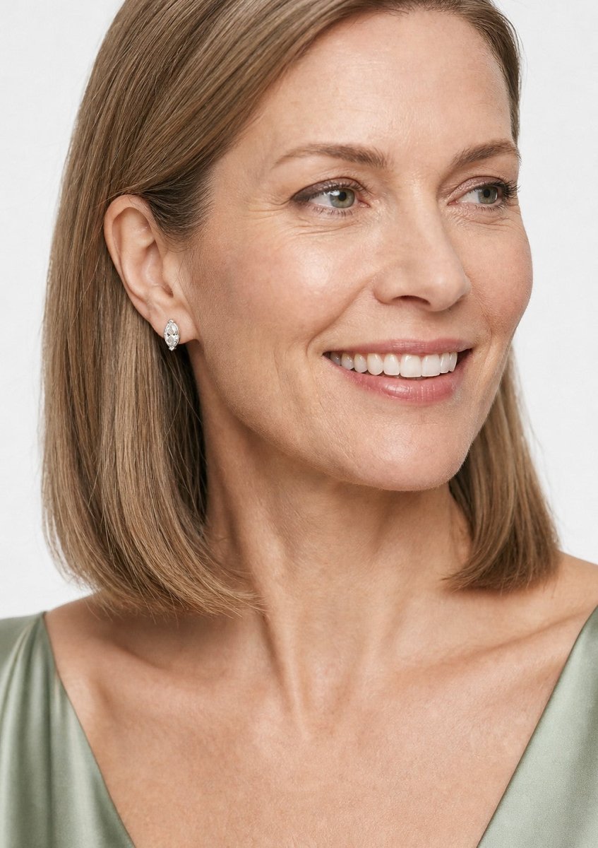 A smiling woman wearing a white gold earrings set with long marquise cut, pointed at both ends diamonds