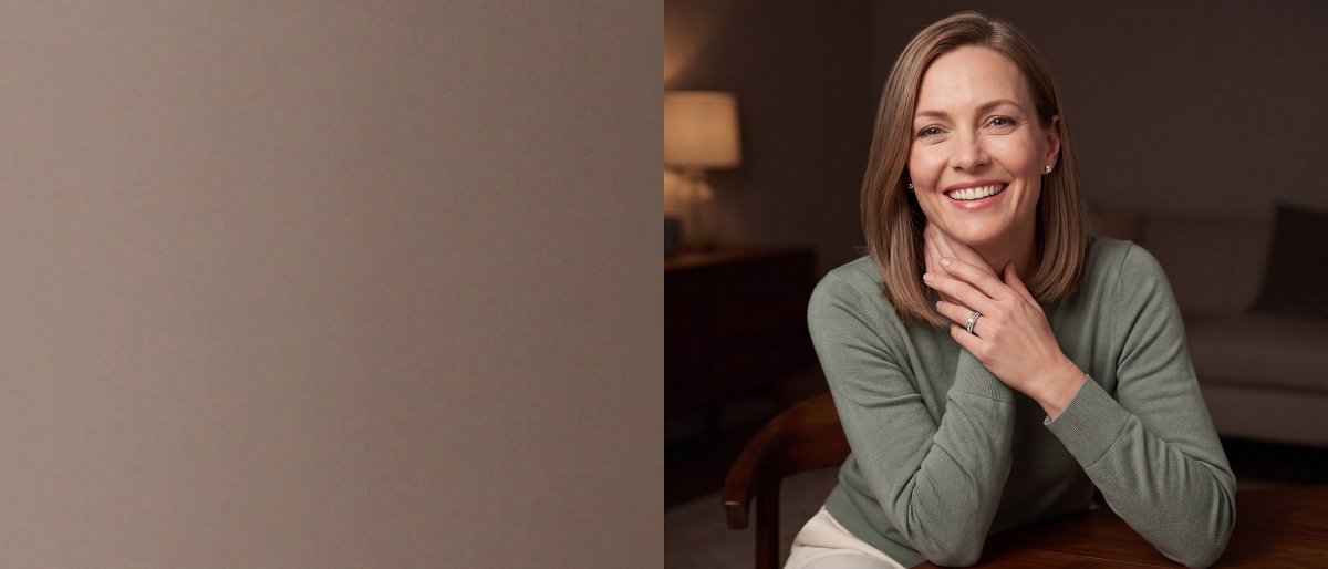 A smiling woman in a sage green sweater with her hands together beneath her chin, wearing a princess cut diamond engagement ring and princess cut diamond stud earrings