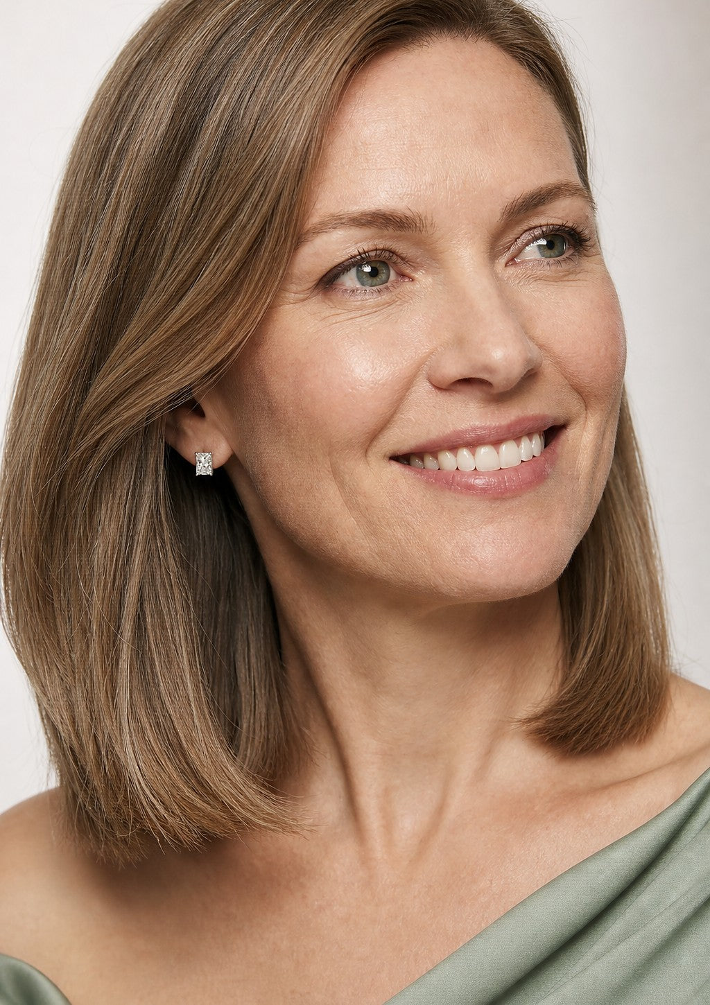 A smiling woman wearing a white gold earrings set with rectangular radiant cut, with trimmed corners diamonds