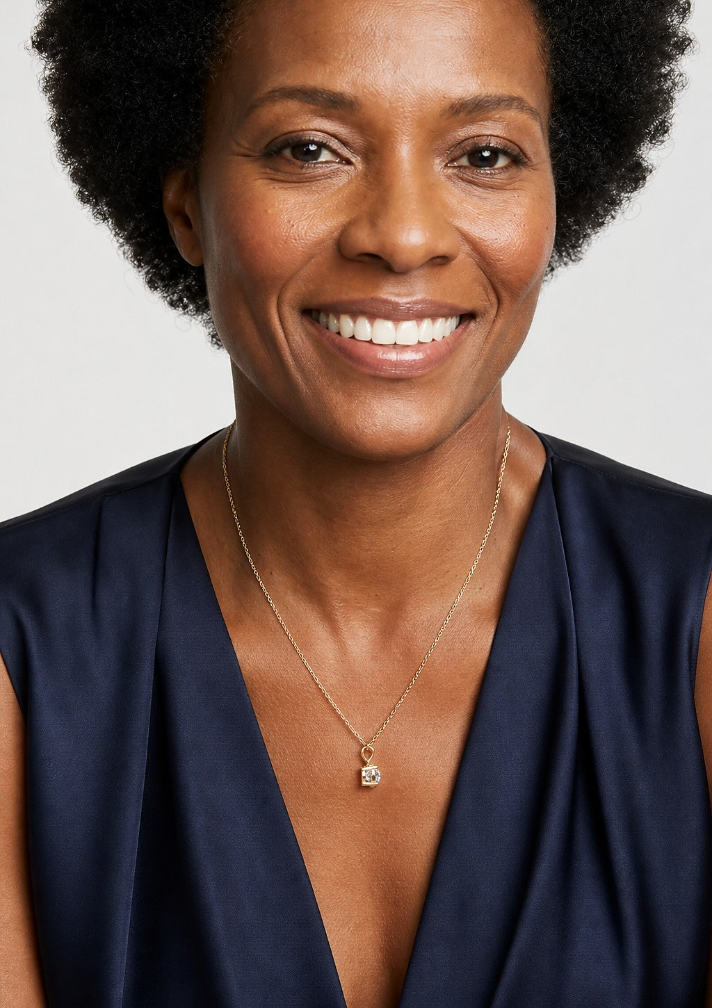 A smiling woman wearing a yellow gold pendant set with rectangular radiant cut, with trimmed corners diamonds
