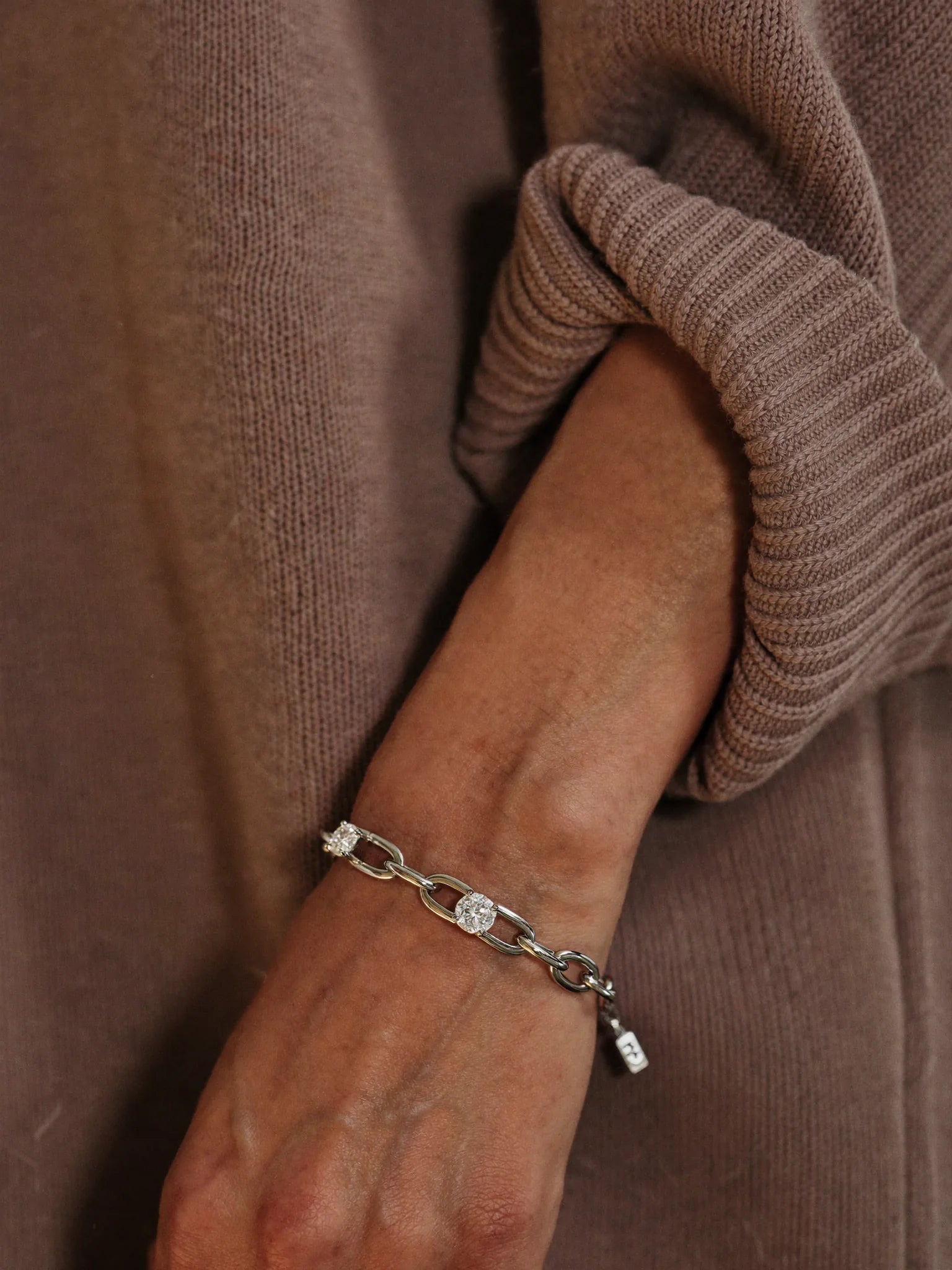 A custom diamond bracelet worn on the wrist with a taupe knit sleeve